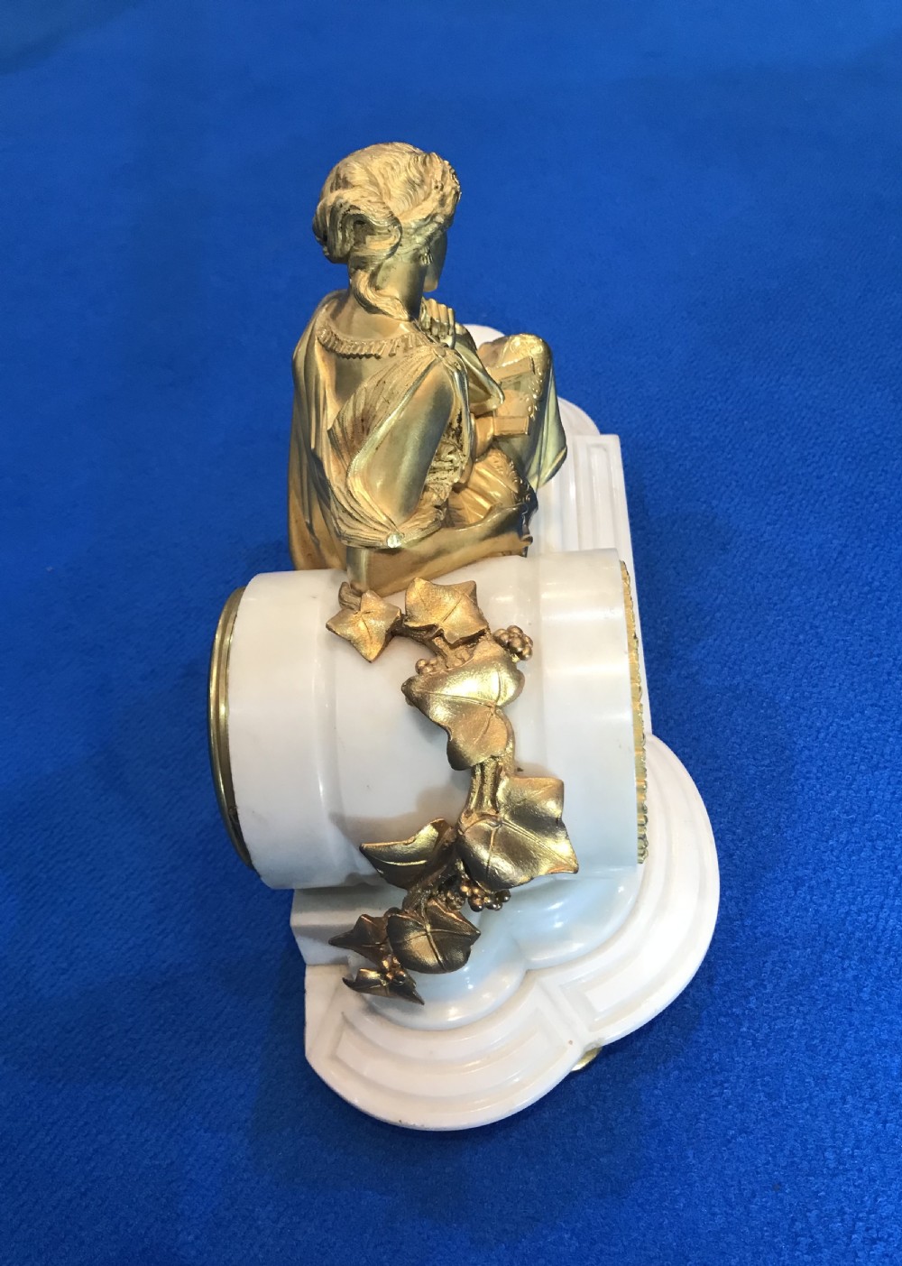 A Victorian gilt bronze and white marble mantel clock featuring a reclining classical female figure reading a book atop a stepped base. View V