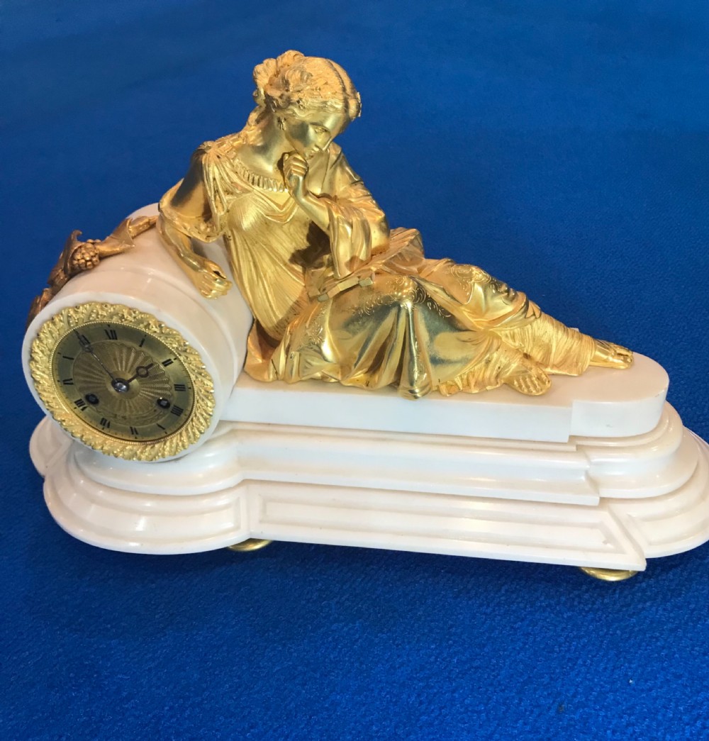 A Victorian gilt bronze and white marble mantel clock featuring a reclining classical female figure reading a book atop a stepped base. View VII