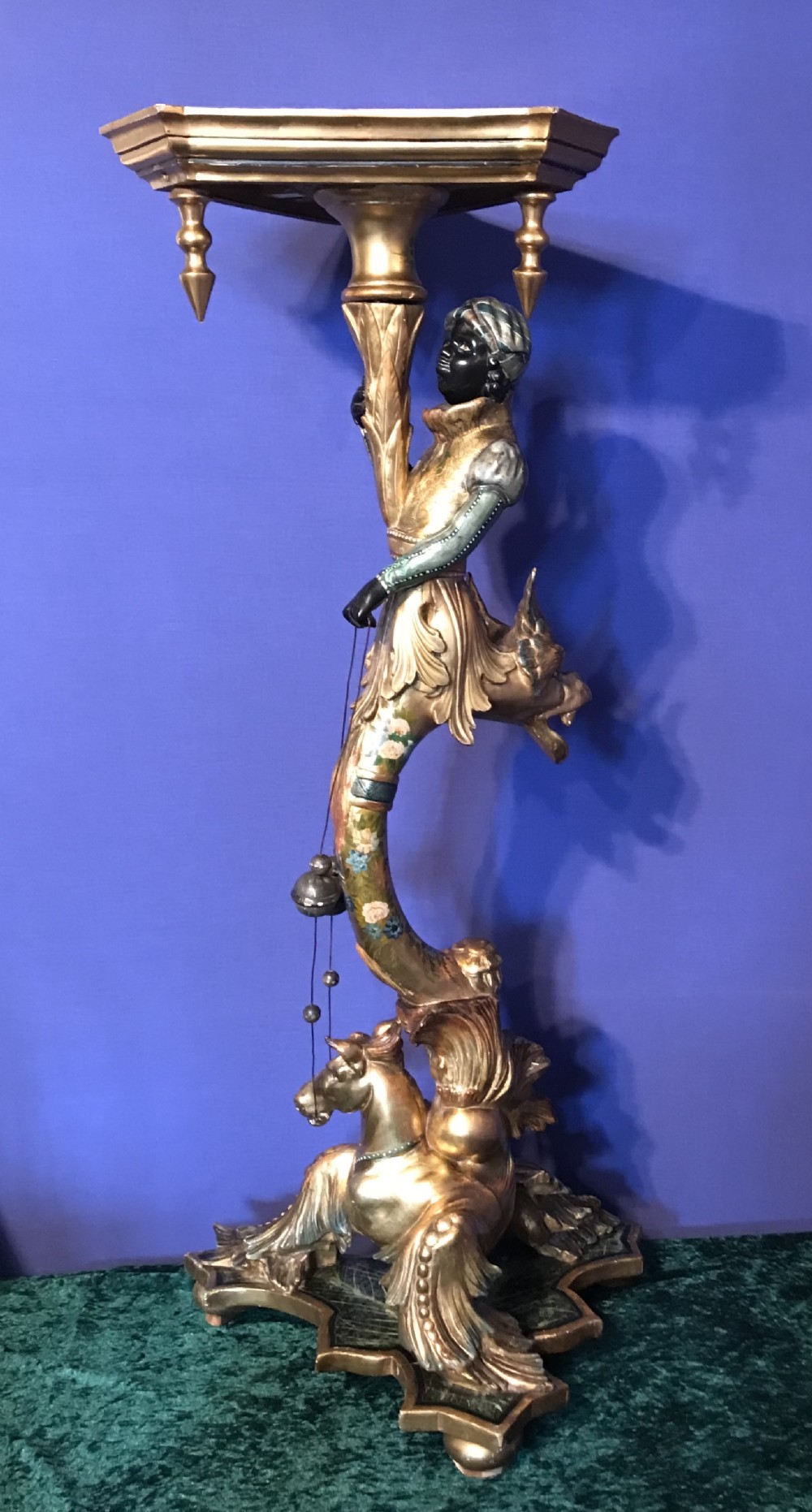 A carved and gilded Venetian torchere pedestal stand featuring a central sculpted figure, floral motifs, and an ornate base.
