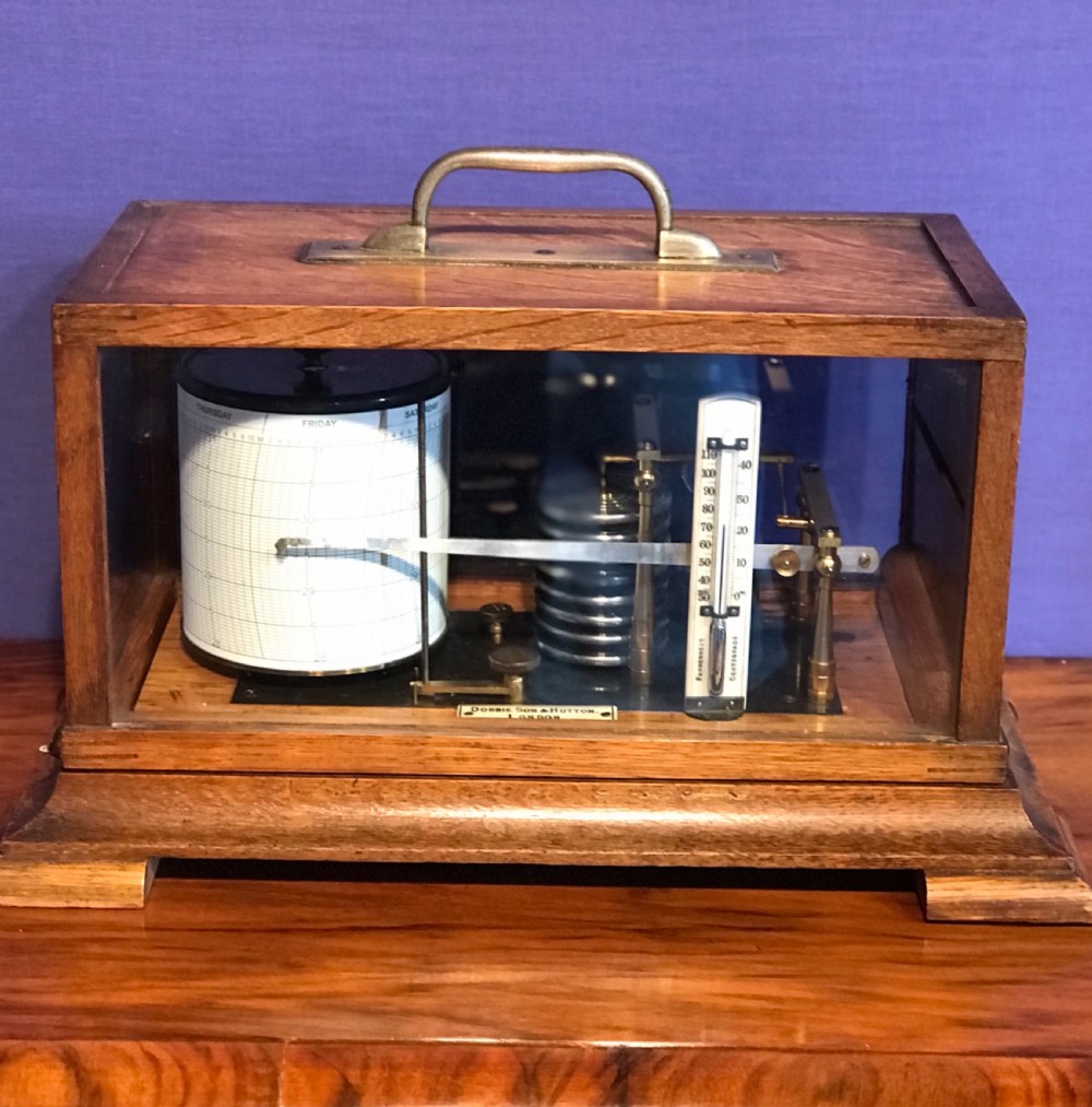 An antique barograph with a brass mechanism and paper recording drum encased in a glazed oak frame topped with a brass handle.