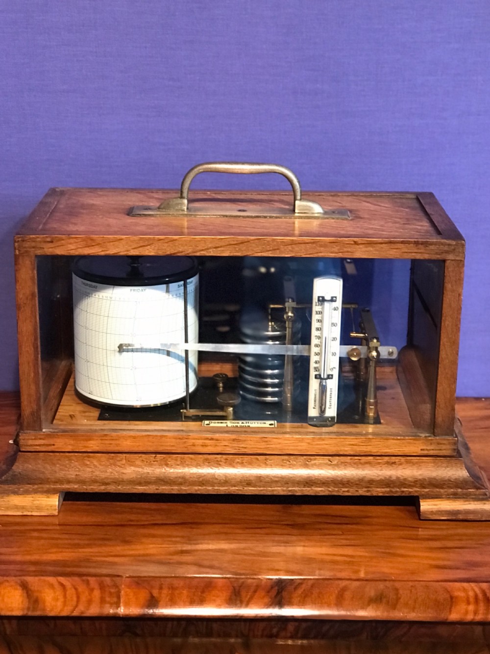 An antique barograph with a brass mechanism and paper recording drum encased in a glazed oak frame topped with a brass handle. View VII