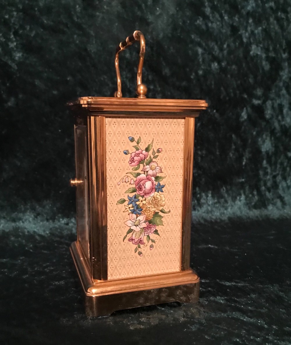 A brass carriage clock with floral enamel side panels, a white dial displaying Roman numerals, and a hinged top handle. View III