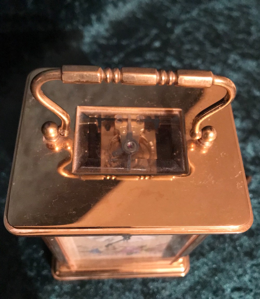 A brass carriage clock with floral enamel side panels, a white dial displaying Roman numerals, and a hinged top handle. View VII