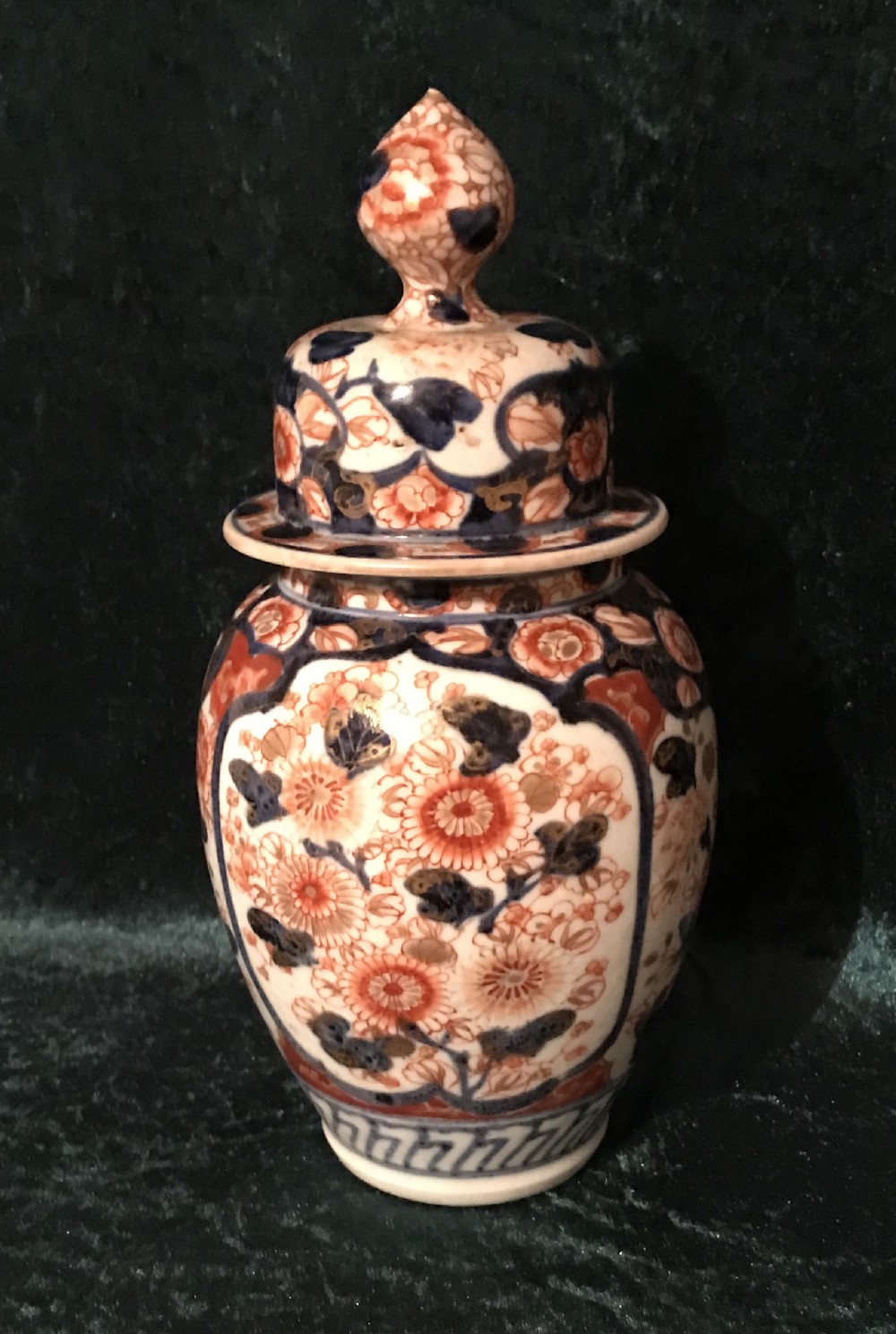 An antique Japanese Imari porcelain lidded vase decorated with intricate orange-red chrysanthemums and cobalt blue floral panels against a white glazed ground.