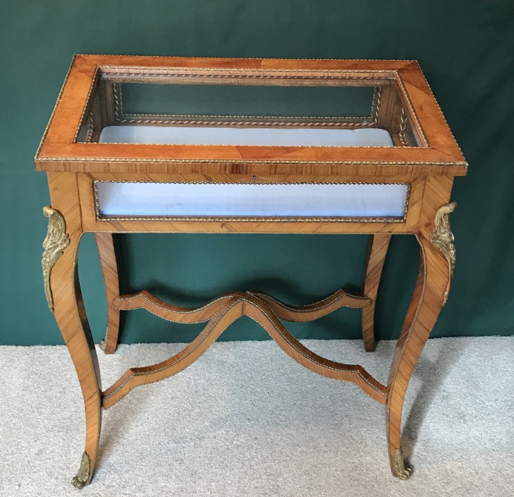 A French-style antique bijouterie table featuring glazed glass sides, parquetry wood veneers, curved cabriole legs with brass mounts, and a cross-shaped stretcher.