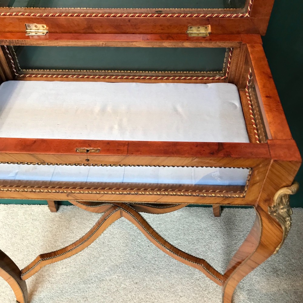 A French-style antique bijouterie table featuring glazed glass sides, parquetry wood veneers, curved cabriole legs with brass mounts, and a cross-shaped stretcher. View IV