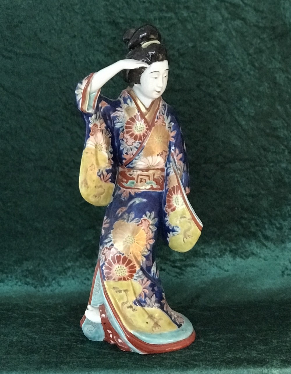 A Japanese Meiji period glazed porcelain figure depicting a standing woman in a hand-painted floral kimono shielding her eyes.