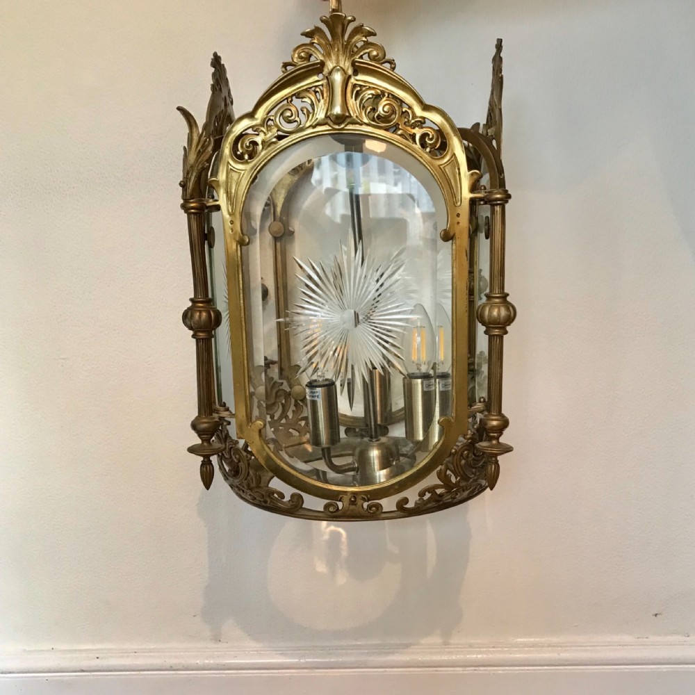 An ornate brass four-sided hall lantern with curved glass panels, starburst glass etchings, and scrolled filigree cresting. View VII