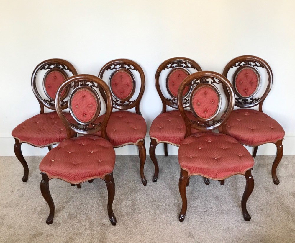 A set of six Victorian carved walnut dining chairs featuring oval balloon backs with button-tufted red upholstery pads and cabriole front legs.