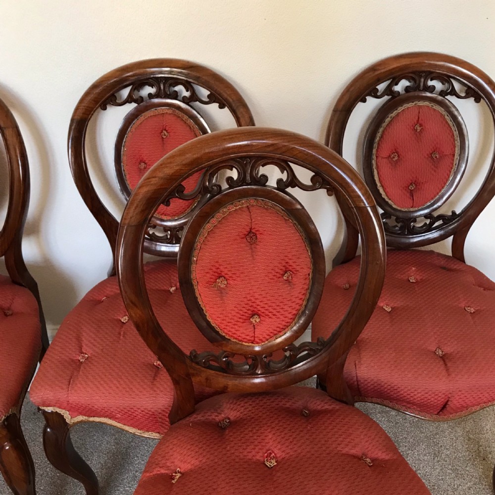 A set of six Victorian carved walnut dining chairs featuring oval balloon backs with button-tufted red upholstery pads and cabriole front legs. View V