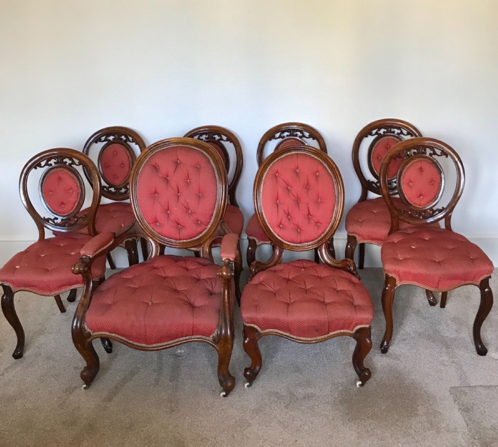 A set of eight Victorian chairs featuring carved dark timber frames, red deep-buttoned fabric upholstery, balloon-shaped backs, and cabriole front legs.