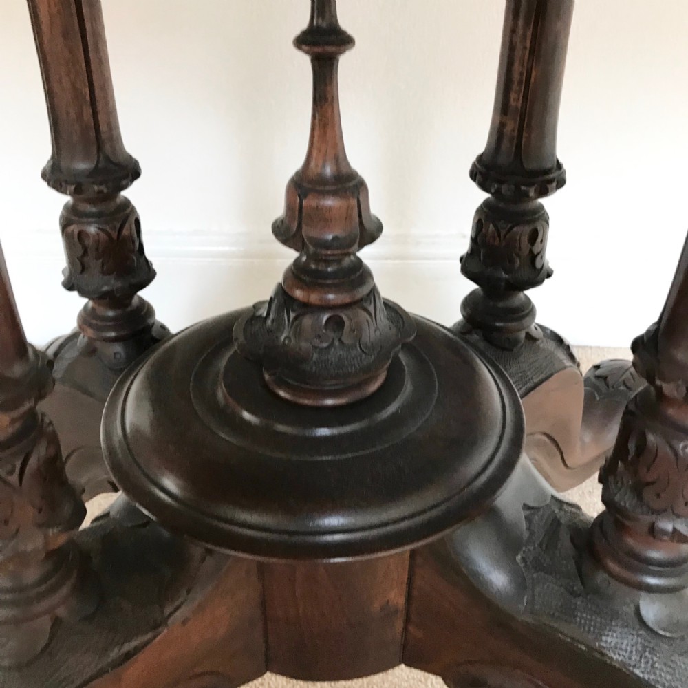 A Victorian tilt-top pedestal table with its circular top locked vertically on a carved wooden base with castors. View V