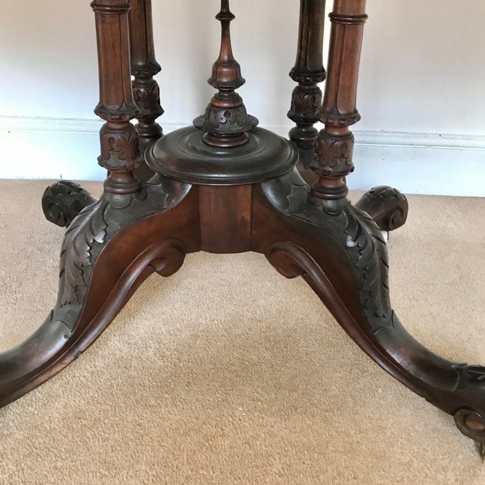 A Victorian tilt-top pedestal table with its circular top locked vertically on a carved wooden base with castors. View VII