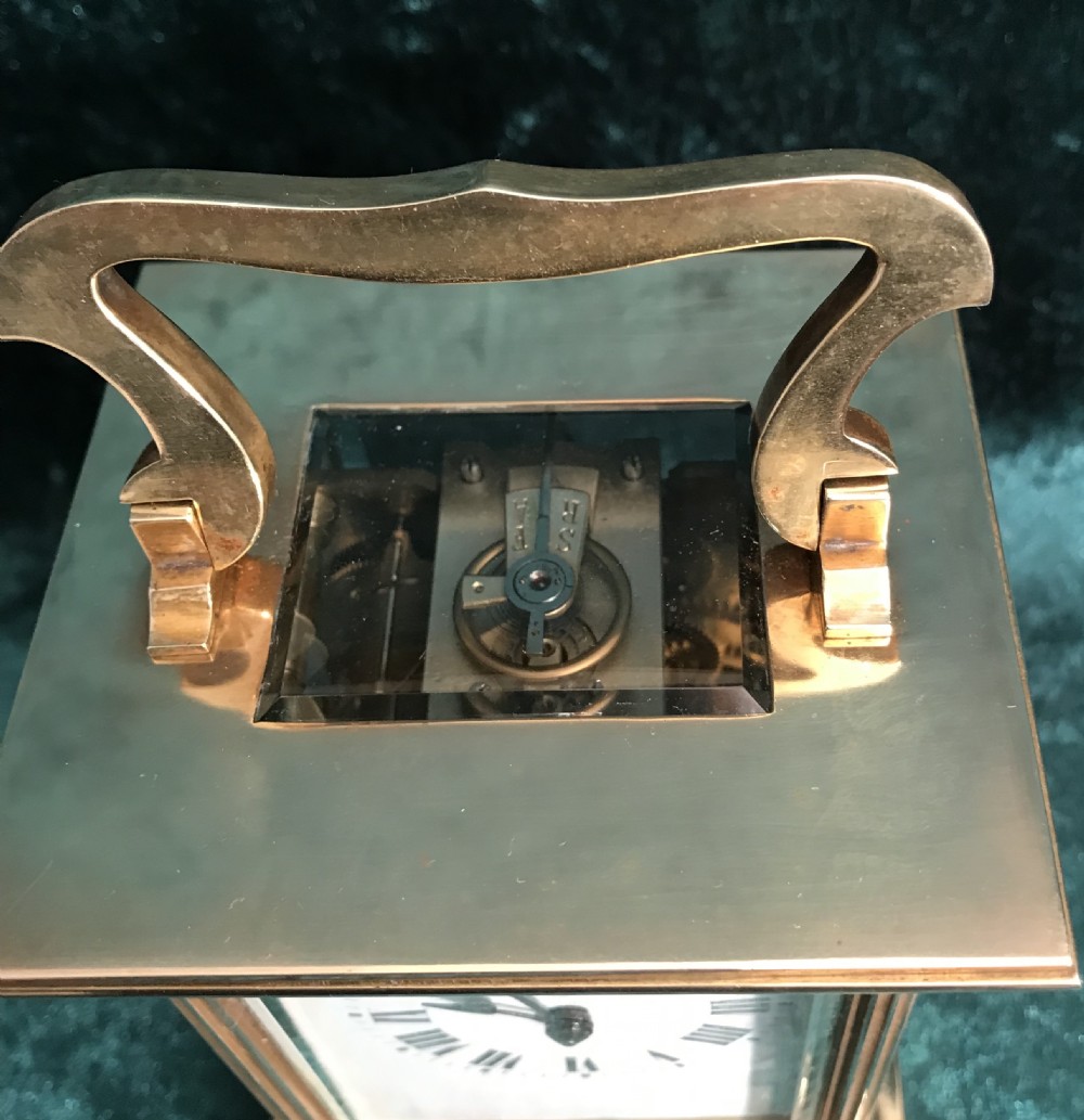 An antique brass carriage clock featuring a top carrying handle, reeded corner columns, and a white enamel dial with black Roman numerals. View II