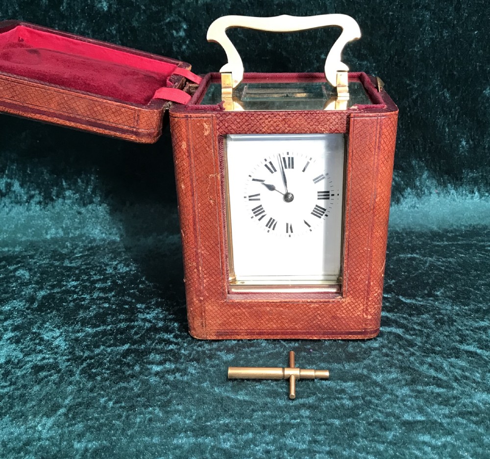 An antique brass carriage clock featuring a top carrying handle, reeded corner columns, and a white enamel dial with black Roman numerals. View VIII