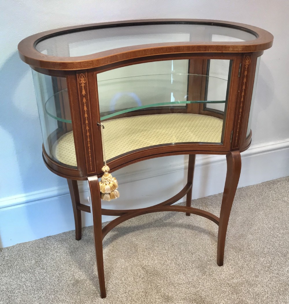An Edwardian kidney-shaped mahogany bijouterie table with glazed top and sides, floral inlay, slender curved legs, and an interior glass shelf.
