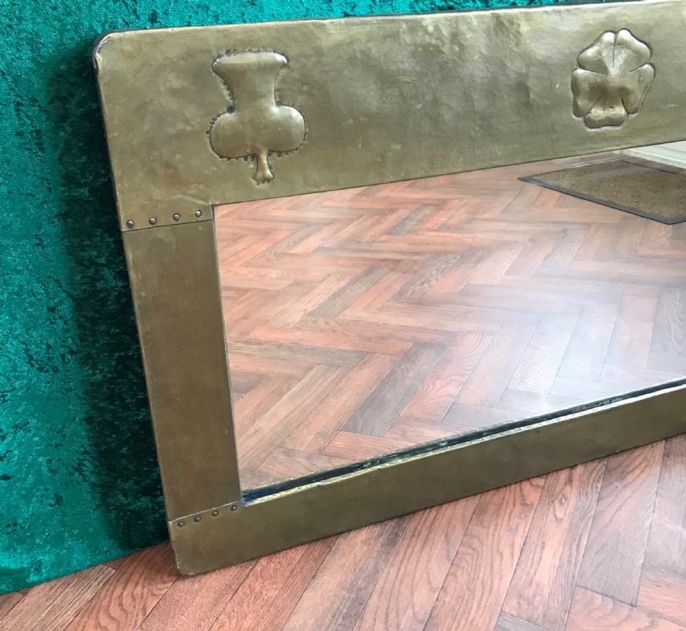 A large rectangular Arts and Crafts wall mirror featuring a hand-hammered brass frame decorated with repousse thistle, rose, and shamrock motifs. View III