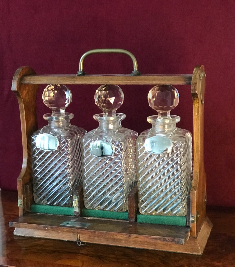 A 1930s oak tantalus with brass mounts and top carrying handle containing three cut glass decanters with round stoppers. View II