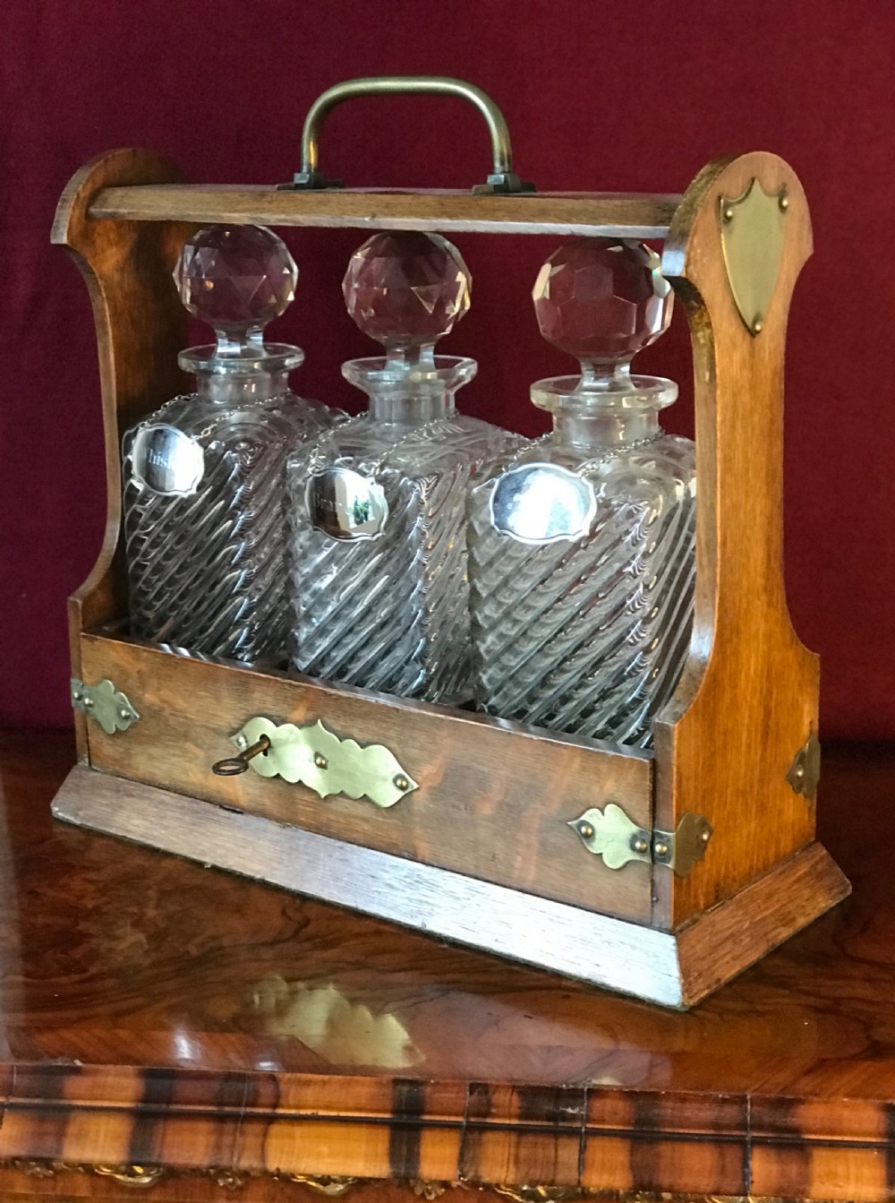 A 1930s oak tantalus with brass mounts and top carrying handle containing three cut glass decanters with round stoppers. View VI