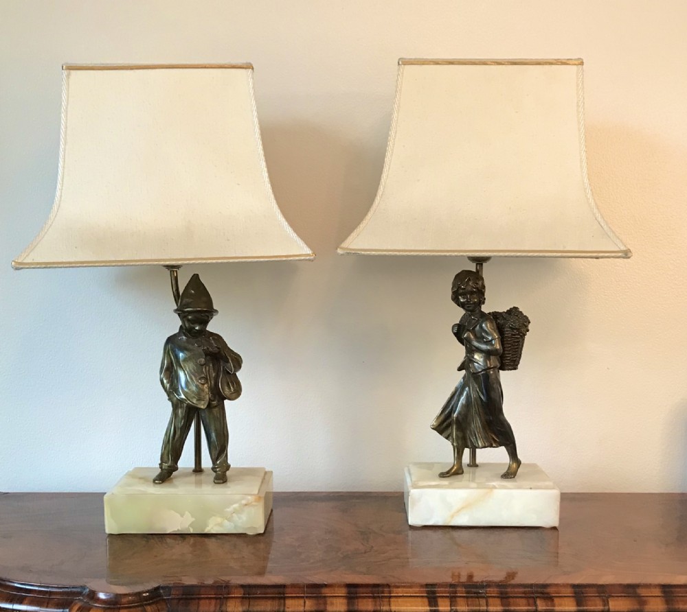 A pair of 1930s Art Deco table lamps featuring bronze figures of a boy and girl standing on rectangular onyx bases beneath flared cream shades.