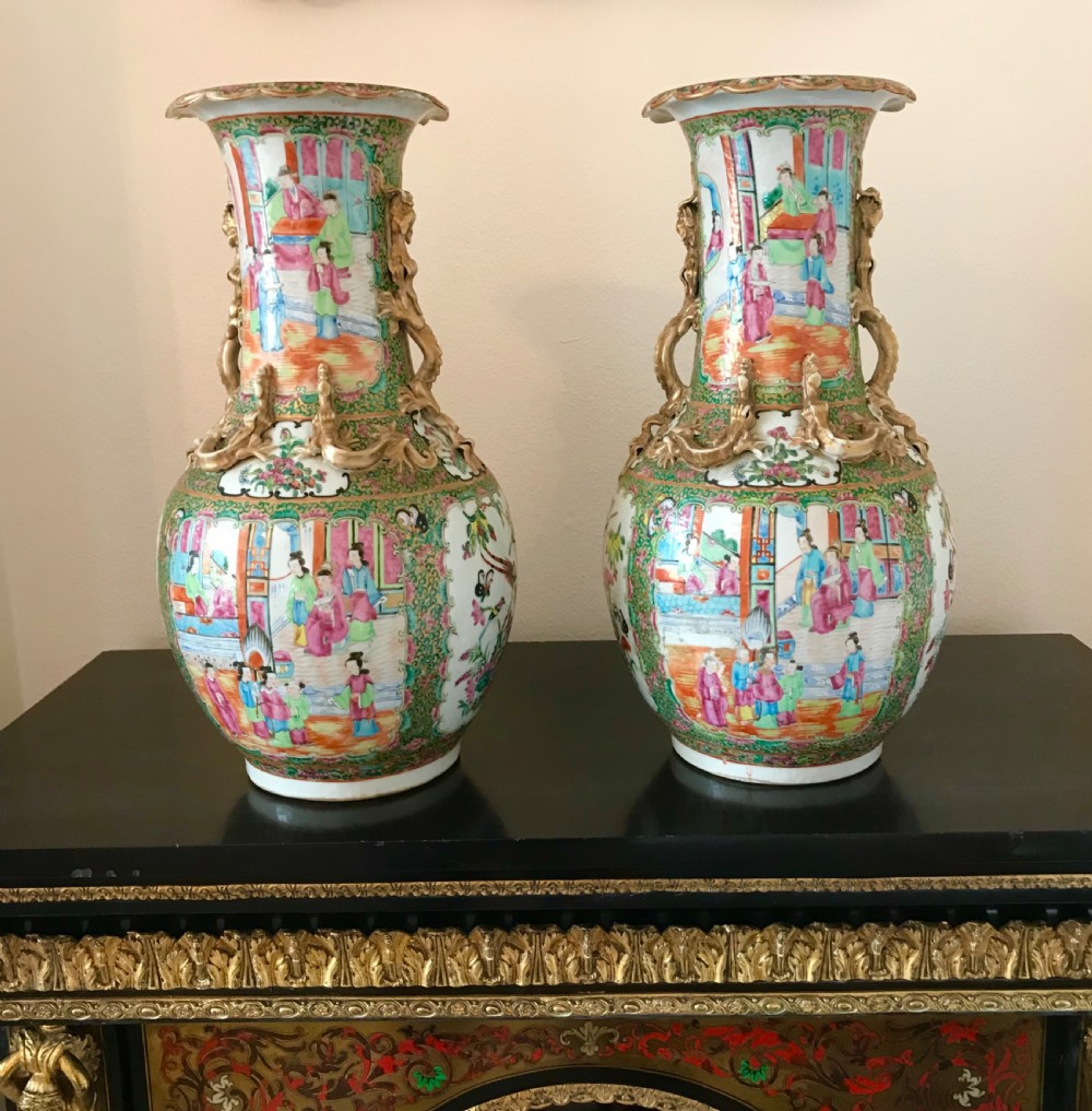 A pair of 19th-century Chinese Canton Famille Rose porcelain baluster vases featuring hand-painted figure panels, floral reserves, and gilded dragon handles.
