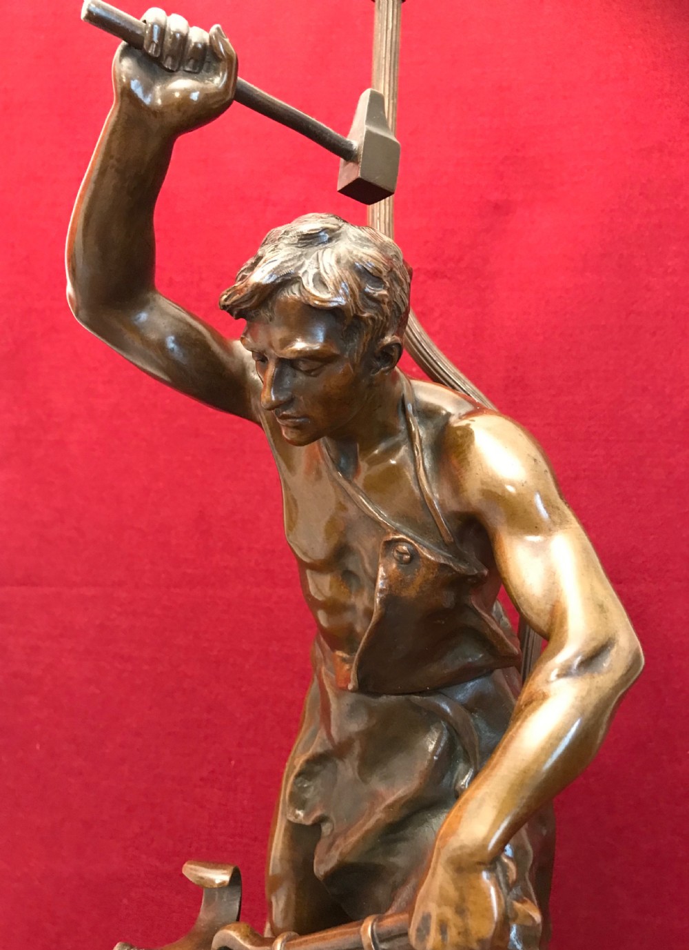 A patinated bronze figural table lamp depicting a muscular blacksmith standing at an anvil holding a hammer and tongs, raised on a moulded circular base. View V