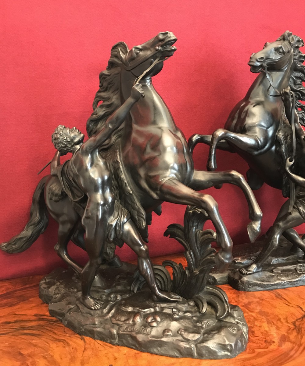 A pair of patinated dark bronze sculptures depicting rearing horses held by grooms on naturalistic bases. View V