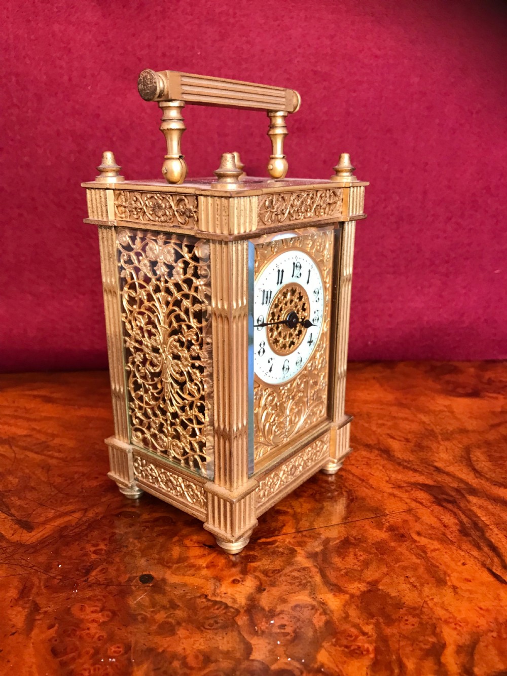 An ornate gilt brass carriage clock featuring pierced filigree side panels, fluted corner columns, top finials, and a white enamel dial with Arabic numerals. View IV