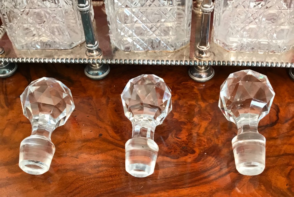 An Edwardian silver-plated metal decanter frame containing three square cut-glass spirit decanters with faceted stoppers and a central raised handle. View IV
