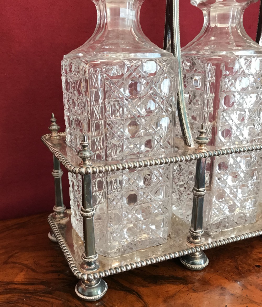 An Edwardian silver-plated metal decanter frame containing three square cut-glass spirit decanters with faceted stoppers and a central raised handle. View VIII
