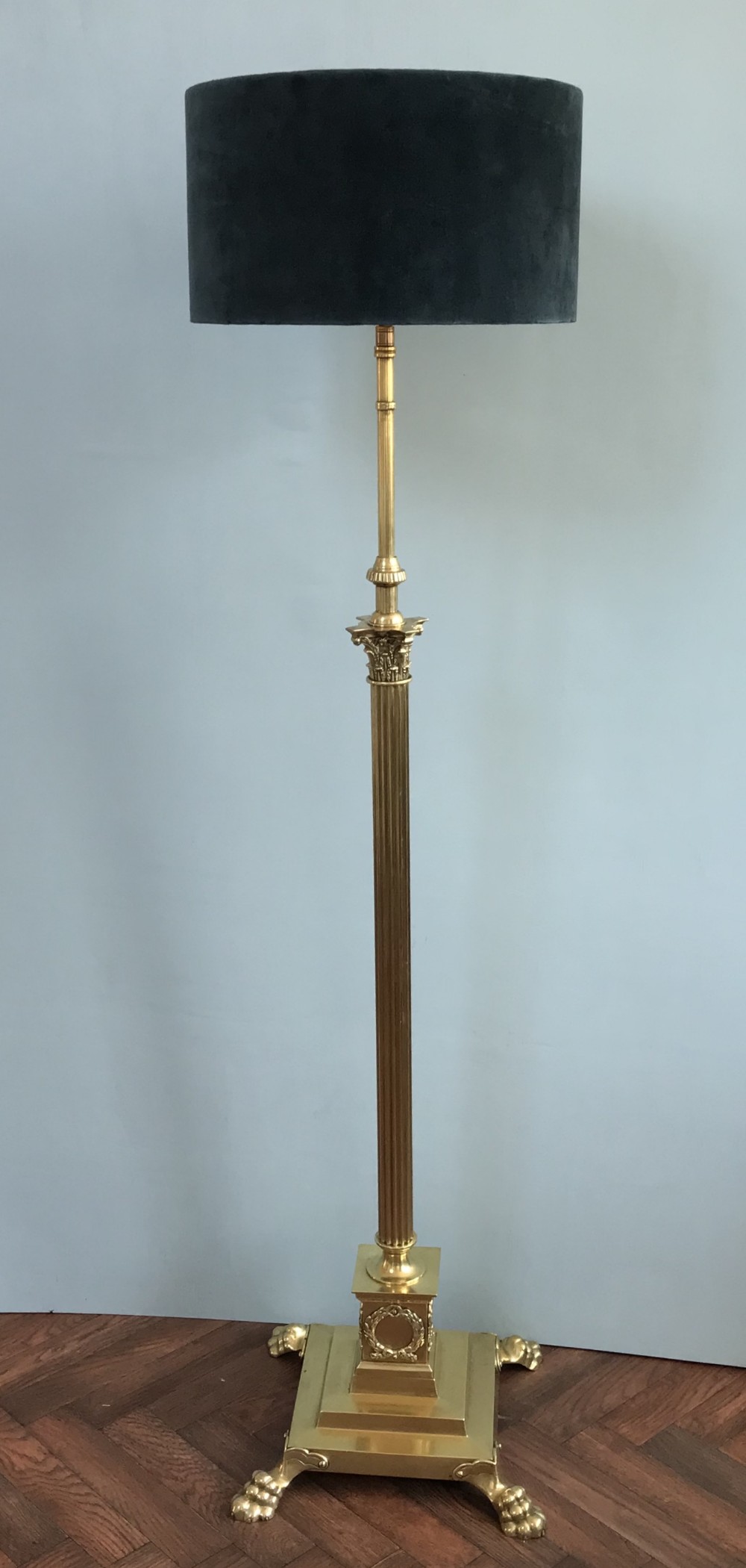 A tall Neoclassical style brass standard lamp featuring a fluted Corinthian column on a square plinth base with paw feet and a dark navy drum shade.