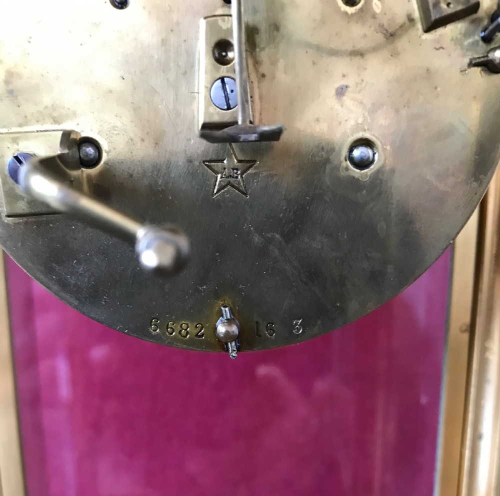 A French four-glass mantel clock featuring a gilt brass case with bevelled glass panels, a white enamel dial with Roman numerals, and a visible pendulum. View V