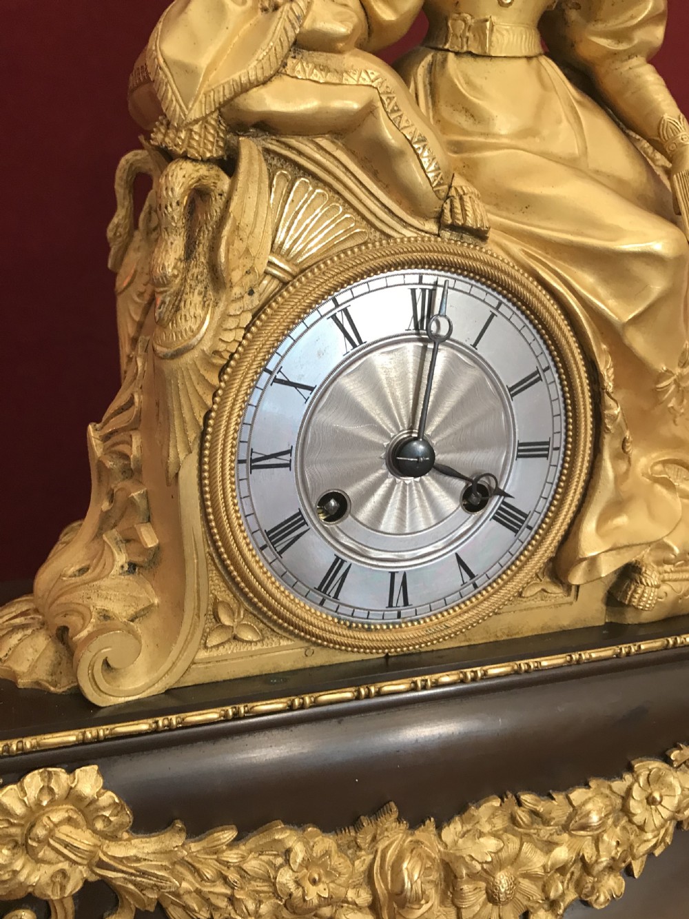 A Regency period gilt bronze figural mantel clock depicting a woman seated beside a circular dial on an ebonised base with decorative swags. View XI