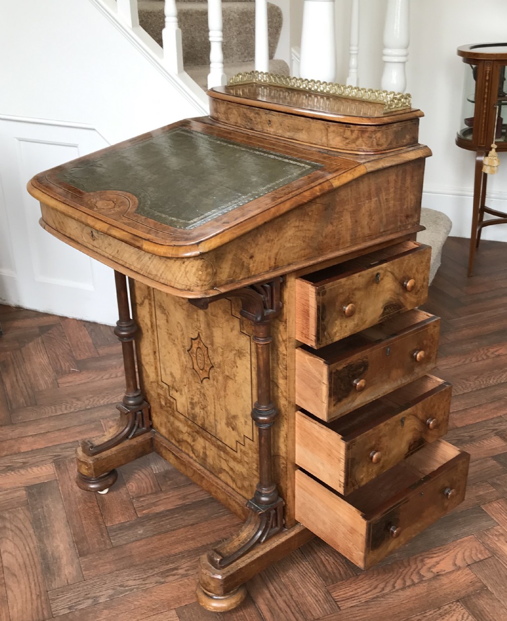A late Victorian burr walnut Davenport desk featuring a sloped green leather writing surface, decorative brass gallery, inlaid side panel, and four side drawers.