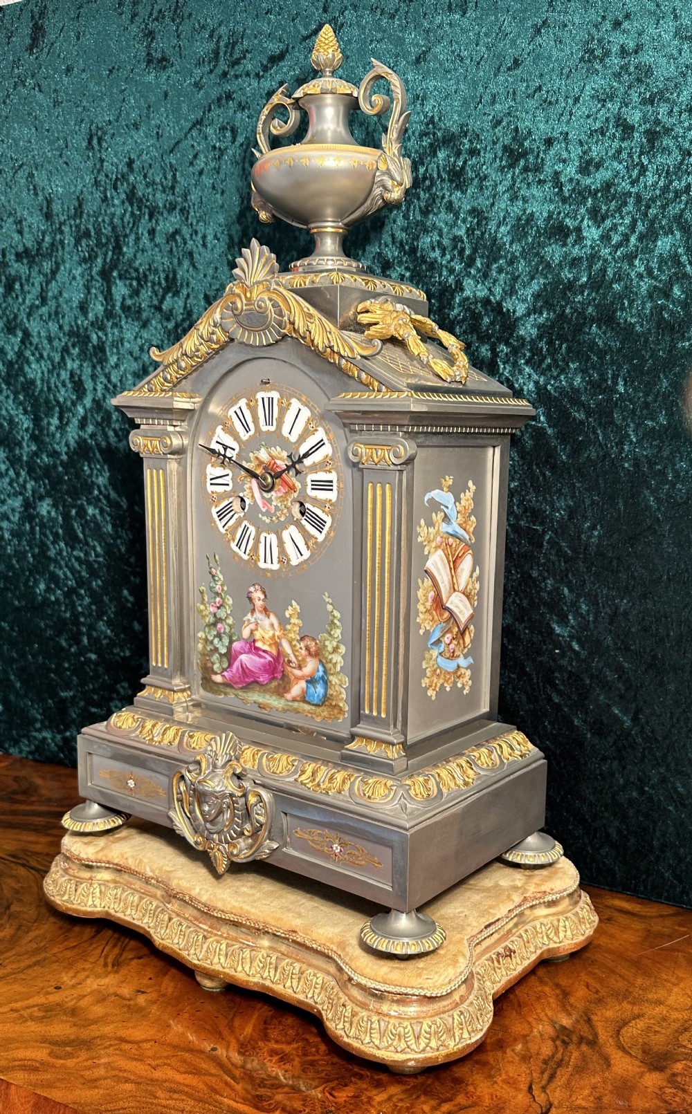 A 19th-century French mantel clock featuring a grey painted metal case decorated with gilded mounts and hand-painted porcelain panels topped with an urn finial.