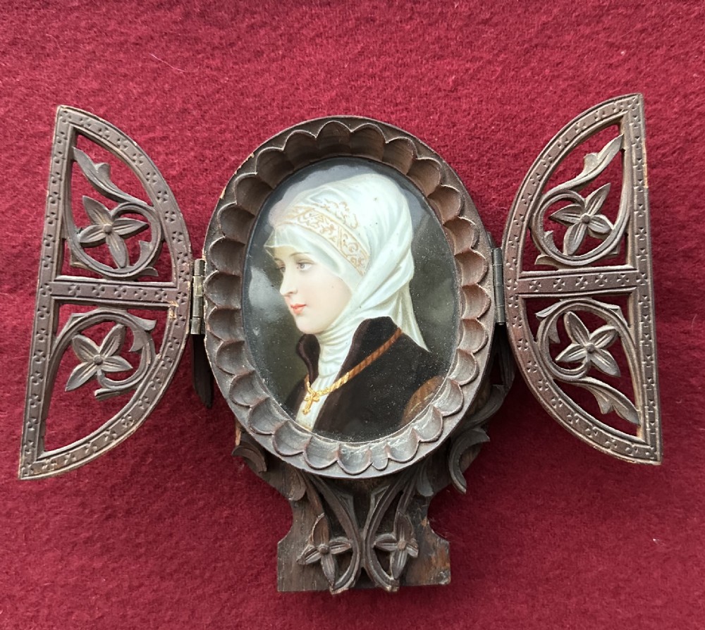 An antique oval portrait miniature depicting a veiled woman housed within a dark carved wooden triptych frame with pierced hinged doors.