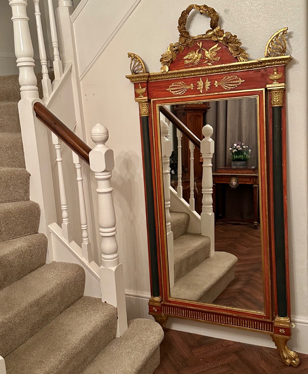 A tall French Empire style giltwood and painted red pier mirror featuring classical columns, a carved bird crest, and lion paw feet.