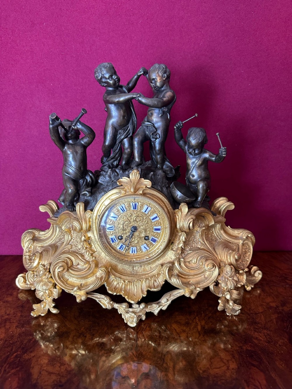 A 19th-century French ormolu mantel clock featuring patinated bronze putti figures atop an ornate gilt bronze rococo base with enamel dial numerals.