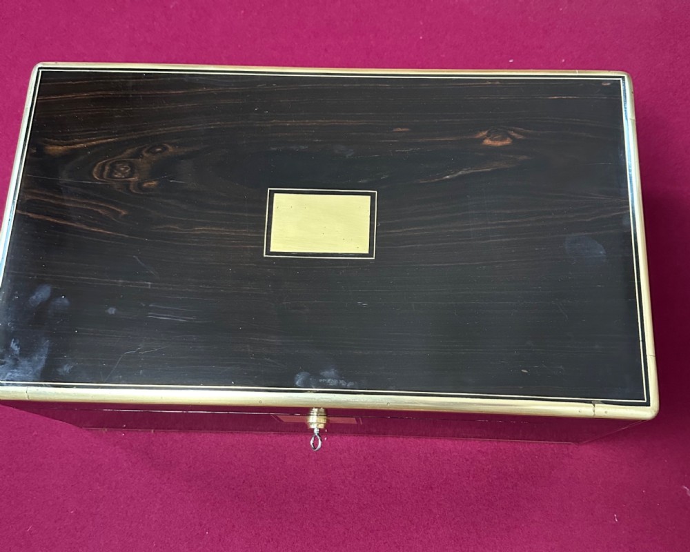 A dark rosewood campaign correspondence box featuring brass edge trim, a central rectangular brass nameplate, and a key inserted into the brass keyhole escutcheon. View III