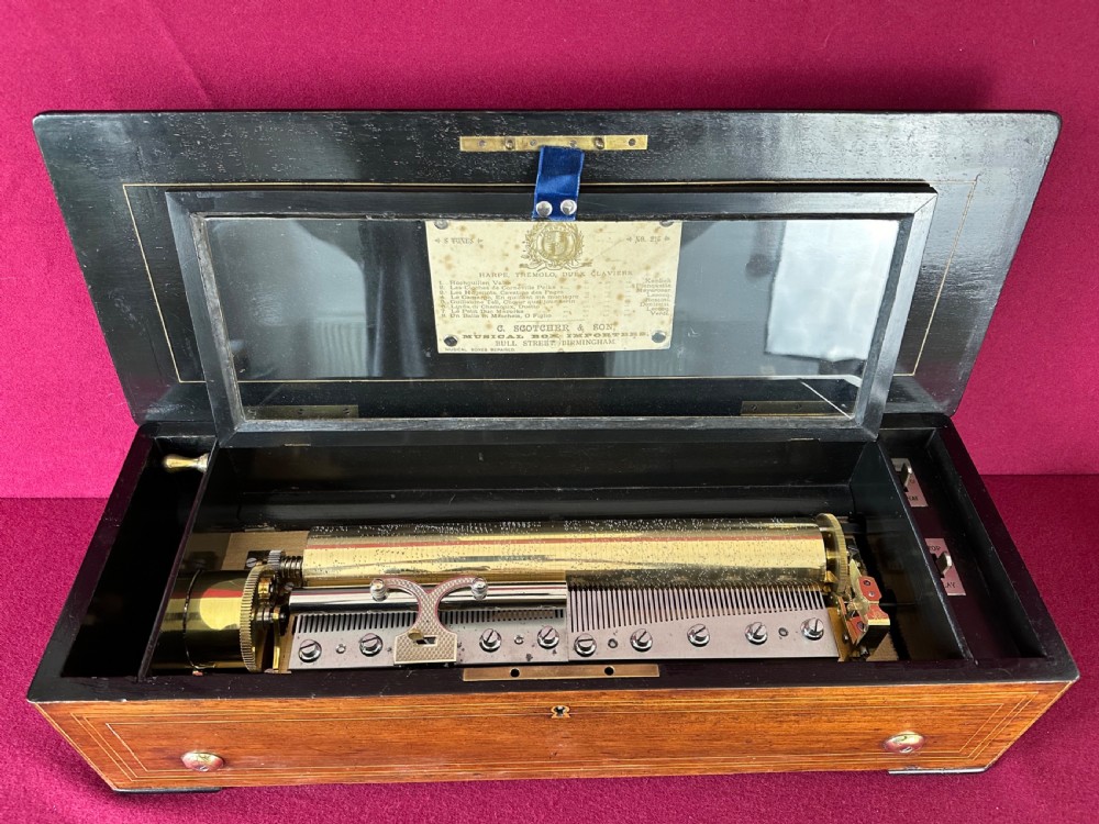 A 19th-century Victorian cylinder music box featuring a wooden case with stringing inlay, an inner glass lid, and a visible brass cylinder mechanical movement.