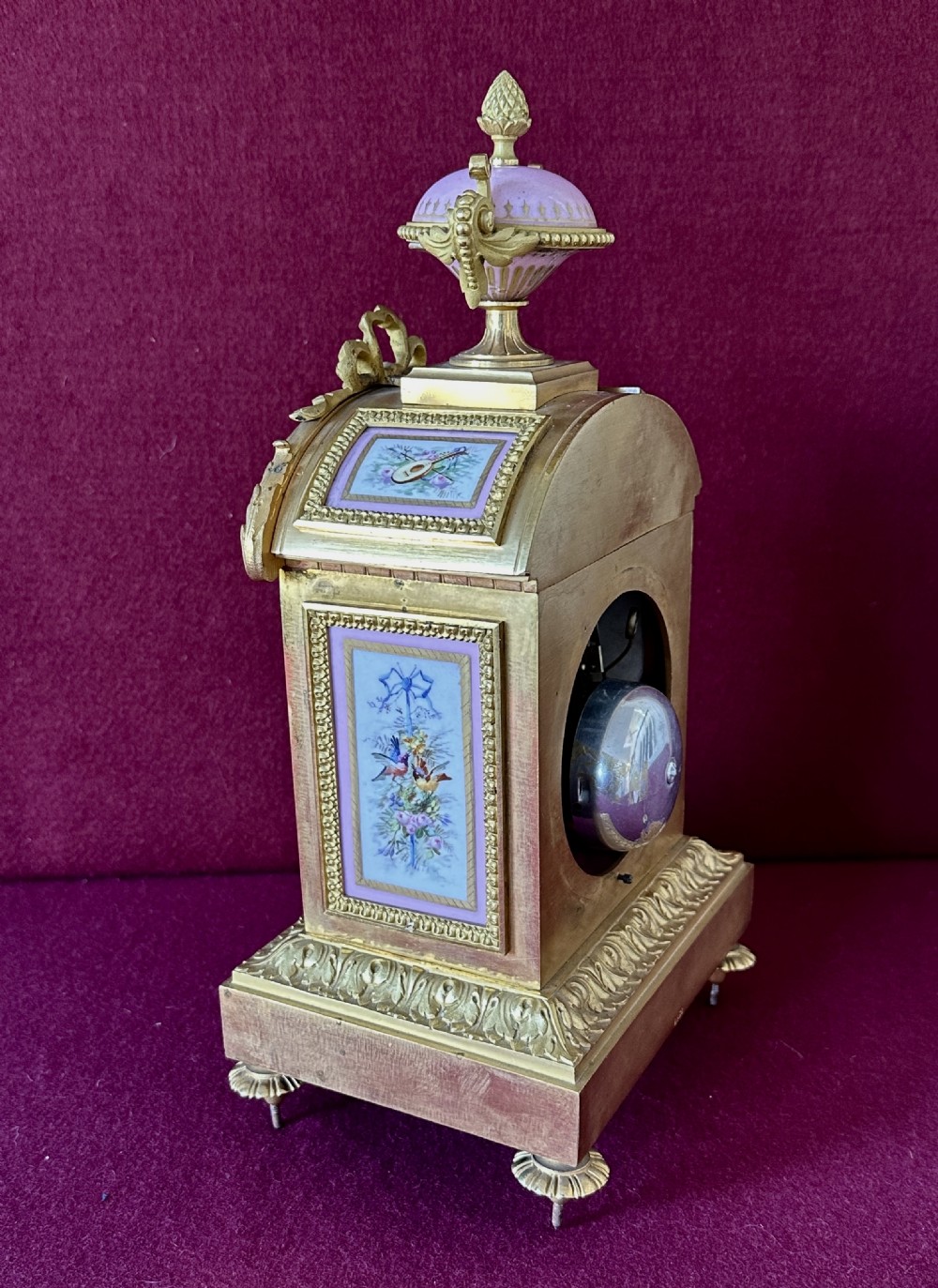 A 19th-century French ormolu mantel clock featuring ornate gilt bronze framing, hand-painted pink porcelain panels with floral motifs, and a matching porcelain urn finial. View IV