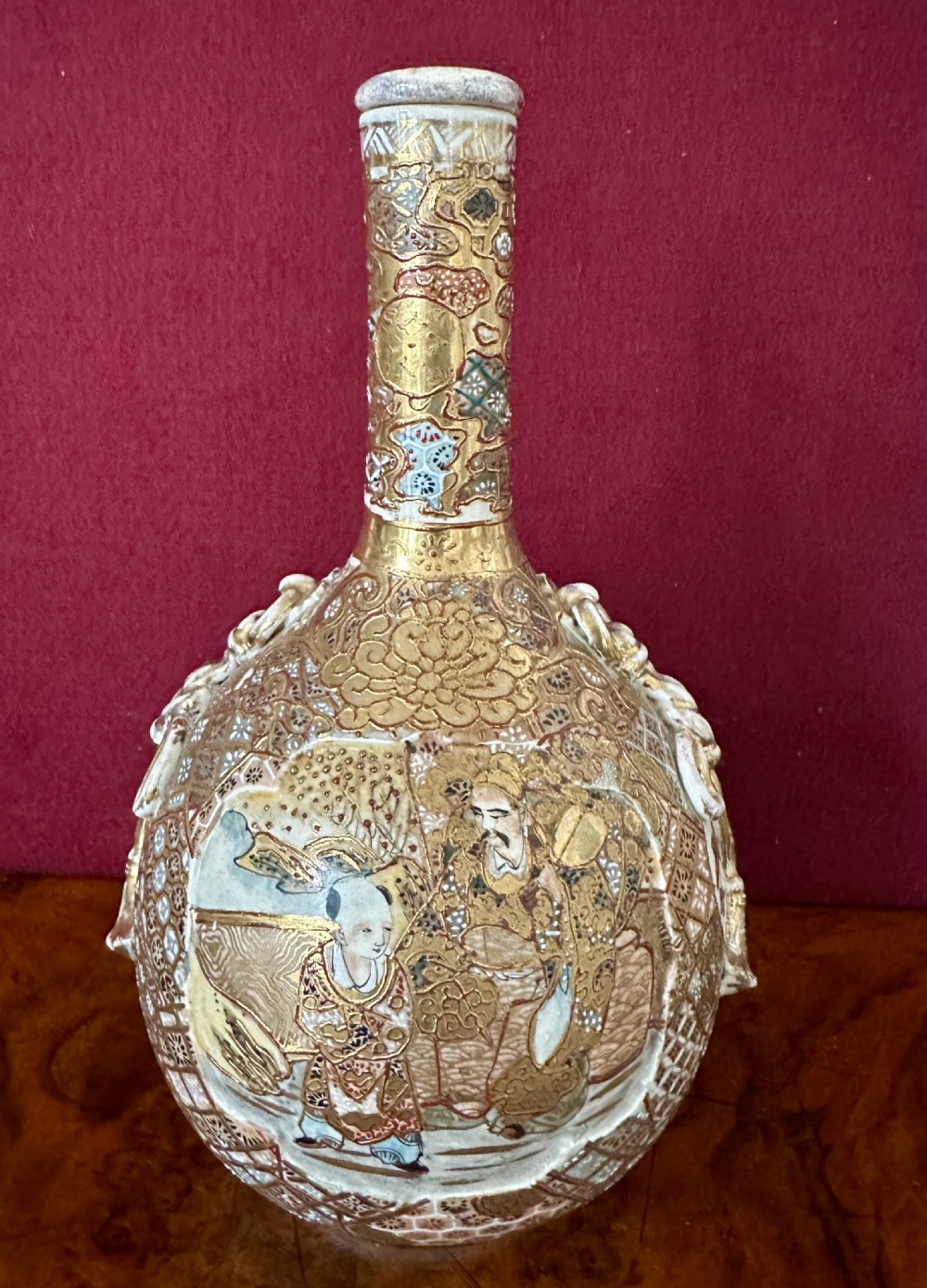 A late 19th-century Japanese Satsuma earthenware bottle vase decorated with intricate hand-painted figures, heavy gilding, and a long slender neck.
