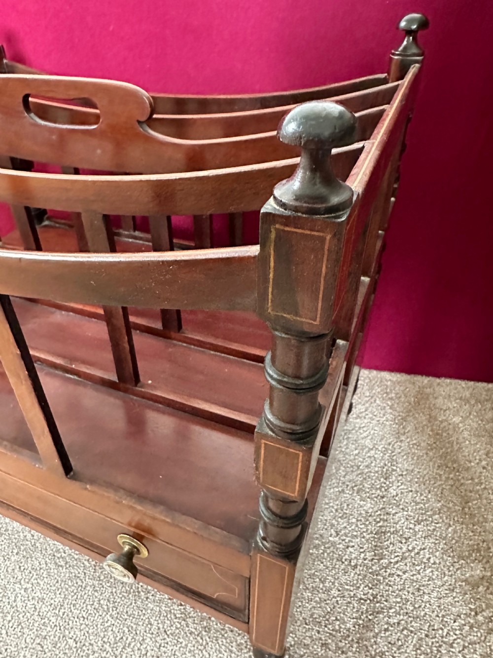 An antique mahogany music canterbury featuring slatted divisions, boxwood inlay, a single lower drawer with brass knobs, and turned legs on castors. View V