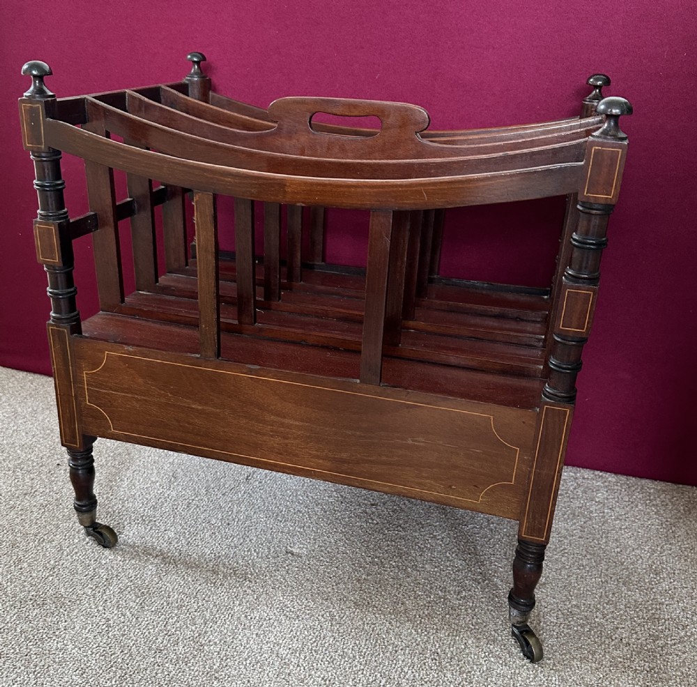 An antique mahogany music canterbury featuring slatted divisions, boxwood inlay, a single lower drawer with brass knobs, and turned legs on castors. View VII