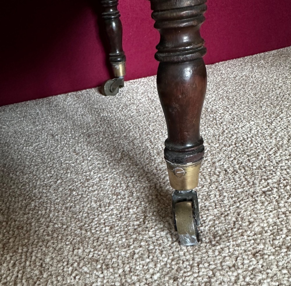 An antique mahogany music canterbury featuring slatted divisions, boxwood inlay, a single lower drawer with brass knobs, and turned legs on castors. View IX