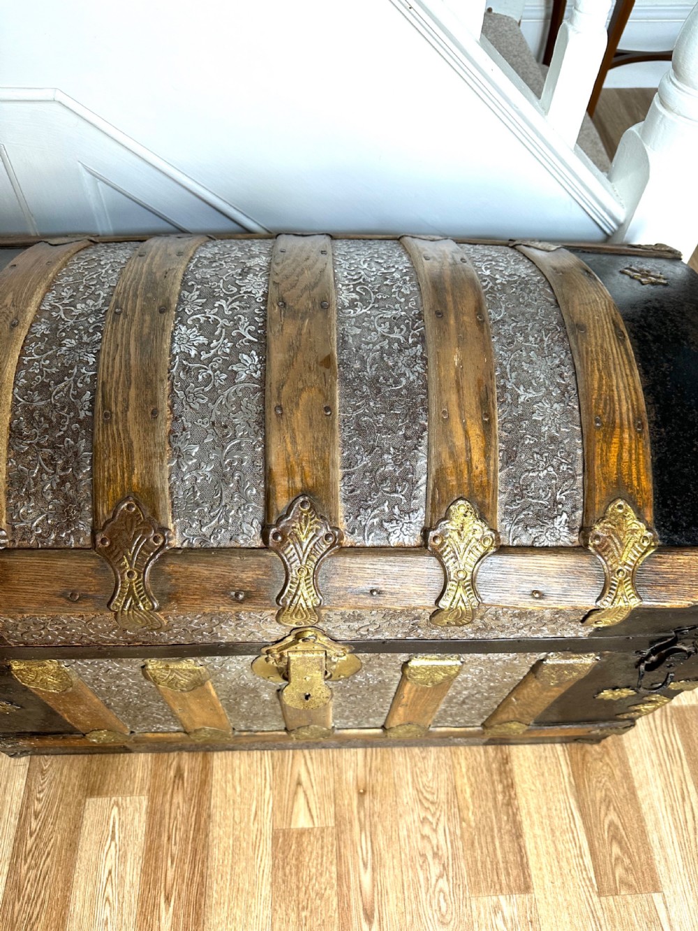 A Victorian dome top travelling trunk featuring embossed patterned metal casing, dark timber reinforcing slats, and brass corner mounts and central lock. View XI
