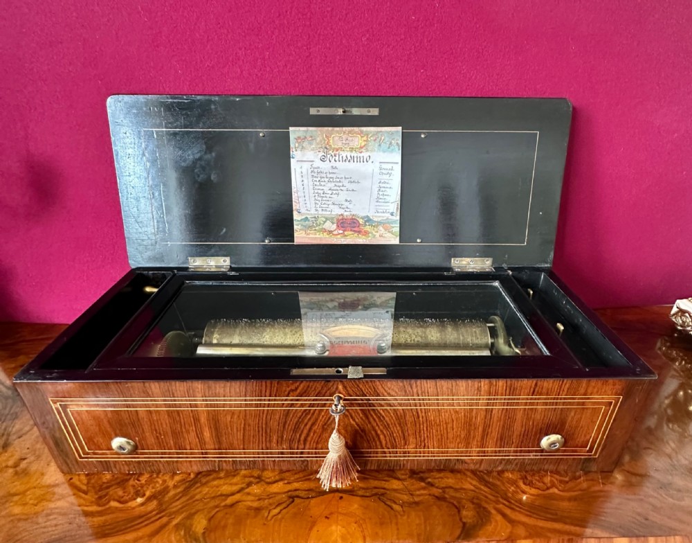 An open Victorian wooden music box featuring boxwood inlay, an ebonised interior lid with a handwritten tune card, and a brass cylinder mechanism beneath an inner glass cover.