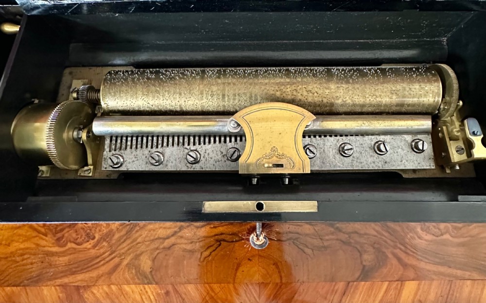 An open Victorian wooden music box featuring boxwood inlay, an ebonised interior lid with a handwritten tune card, and a brass cylinder mechanism beneath an inner glass cover. View III
