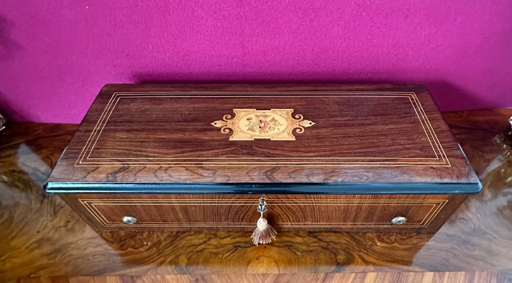 An open Victorian wooden music box featuring boxwood inlay, an ebonised interior lid with a handwritten tune card, and a brass cylinder mechanism beneath an inner glass cover. View V