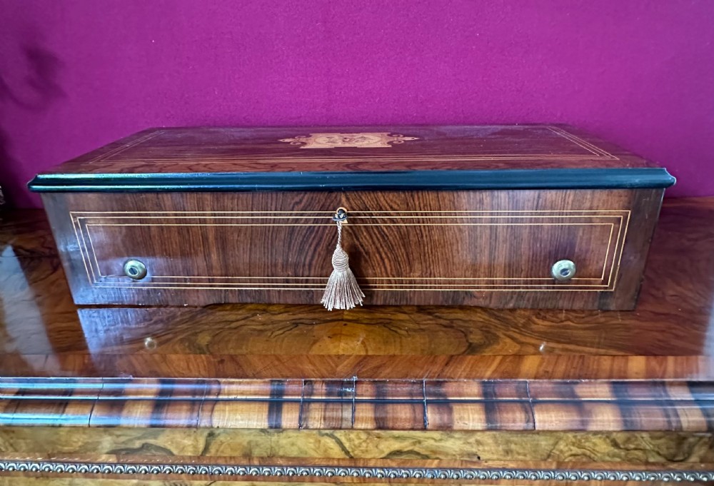 An open Victorian wooden music box featuring boxwood inlay, an ebonised interior lid with a handwritten tune card, and a brass cylinder mechanism beneath an inner glass cover. View VI